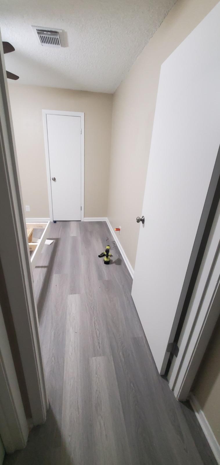 Gray wood-look plank flooring running the length of a hallway, with freshly painted white doors and baseboards on either side.