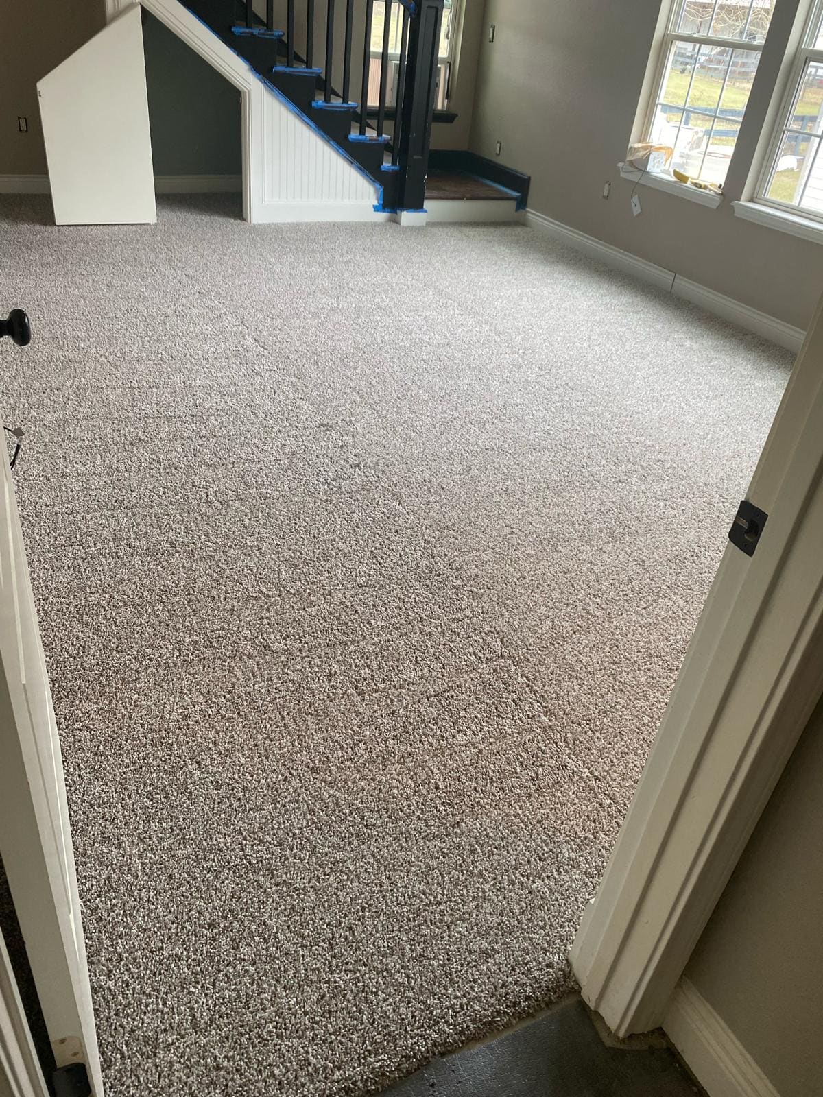 New light gray carpet laid across a living area next to a staircase with black-painted treads and a white beadboard skirt.